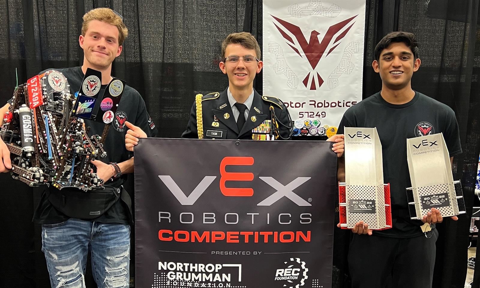Three boys hold up a robot and a championship banner.